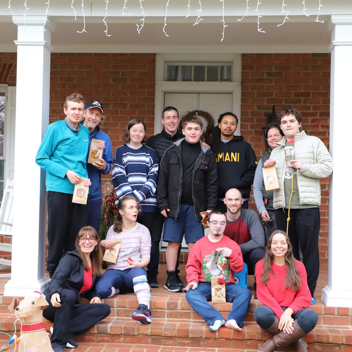 Group gathered on a front porch holding gifts and smiling
